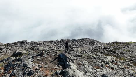 man on bakkanosi cliff raises hands in celebration, overlooking naeroyfjord covered in clouds. drone orbits with parallax effect