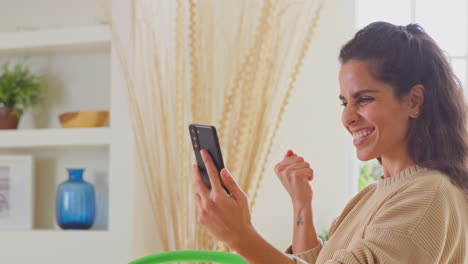 Celebrating-Woman-At-Home-With-Mobile-Phone-Getting-Good-News