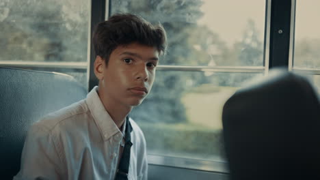 Pensive-Indian-boy-sitting-at-school-bus-window-closeup.-Pupil-looking-camera.