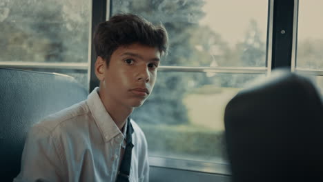 pensive indian boy sitting at school bus window closeup. pupil looking camera.