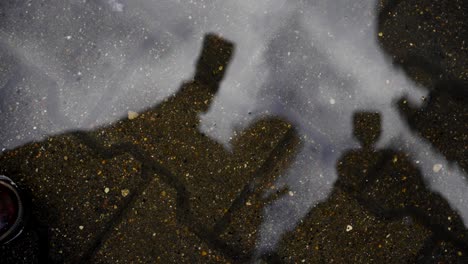 bizarre reflections of two people in a puddle on the sidewalk. abstract shapes
