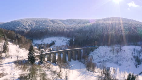 train driving over a stone railway viaduct over a winter countryside