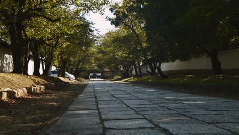 Slide-shot-of-a-stone-path-in-a-temple-with-a-car-in-the-distance-in-Kyoto,-Japan-4K-slow-motion