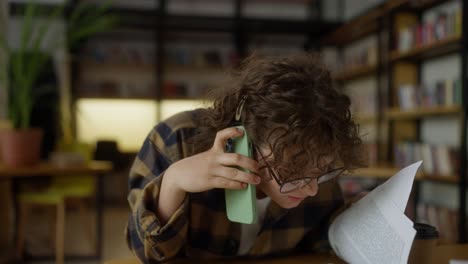 Confident-girl-student-with-curly-hair-communicates-on-the-phone-while-sitting-at-a-table-in-the-library