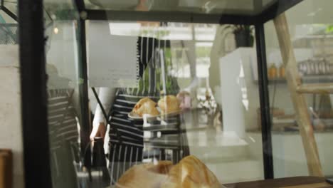 happy biracial female barista taking croissants on plate from display at cafe