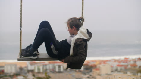 pensive boy swinging alone against the ocean coast