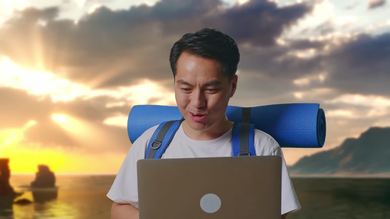Close-up van Aziatische mannelijke wandelaar met bergbeklimmersrugzak die naar een laptop kijkt en wow zegt op het strand