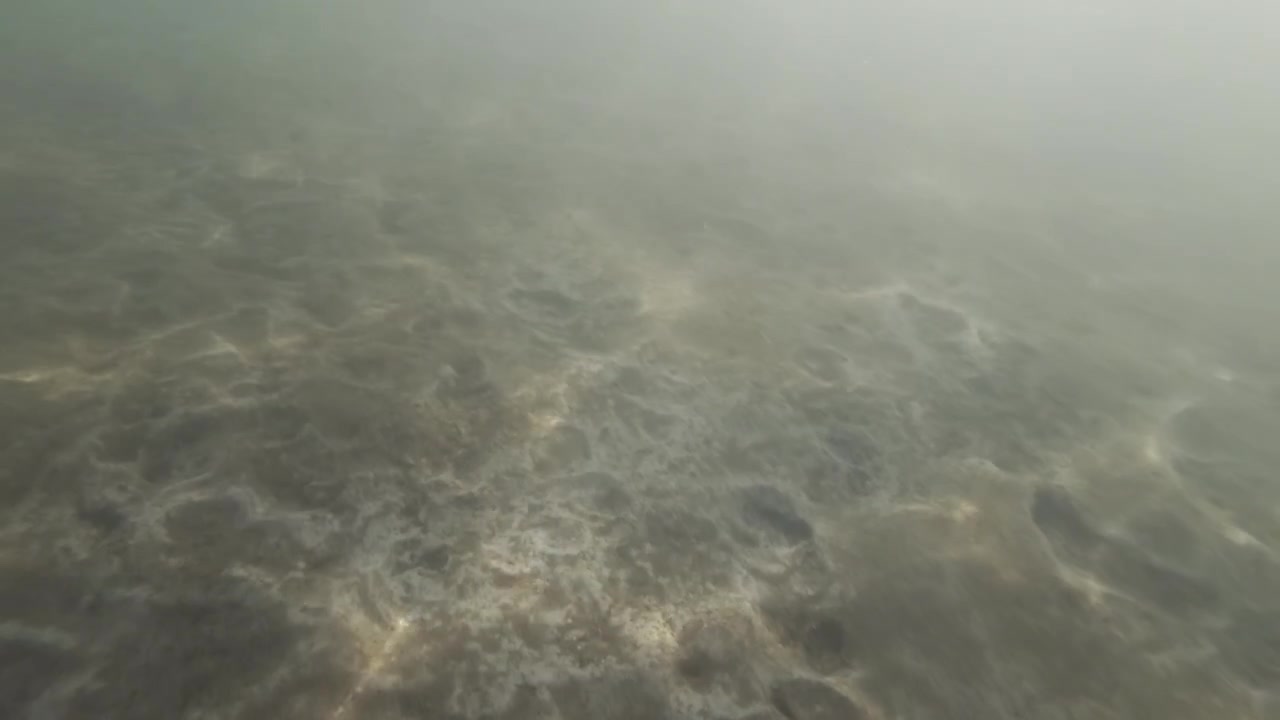 Murky underwater riverbed with sediment and silt, depicting abstract light patterns filtering through the water