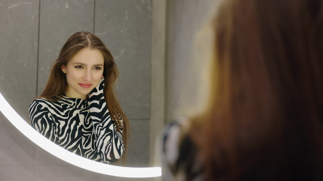 Donna che si guarda in uno specchio moderno del bagno.