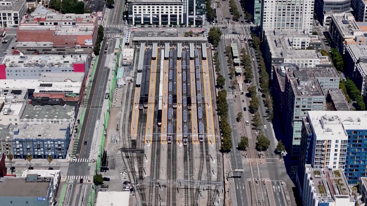 Una vista aérea descendente de la estación Caltrain en San Francisco, capturando las vías de tren organizadas, los trenes estacionados, las carreteras circundantes y los edificios cercanos.