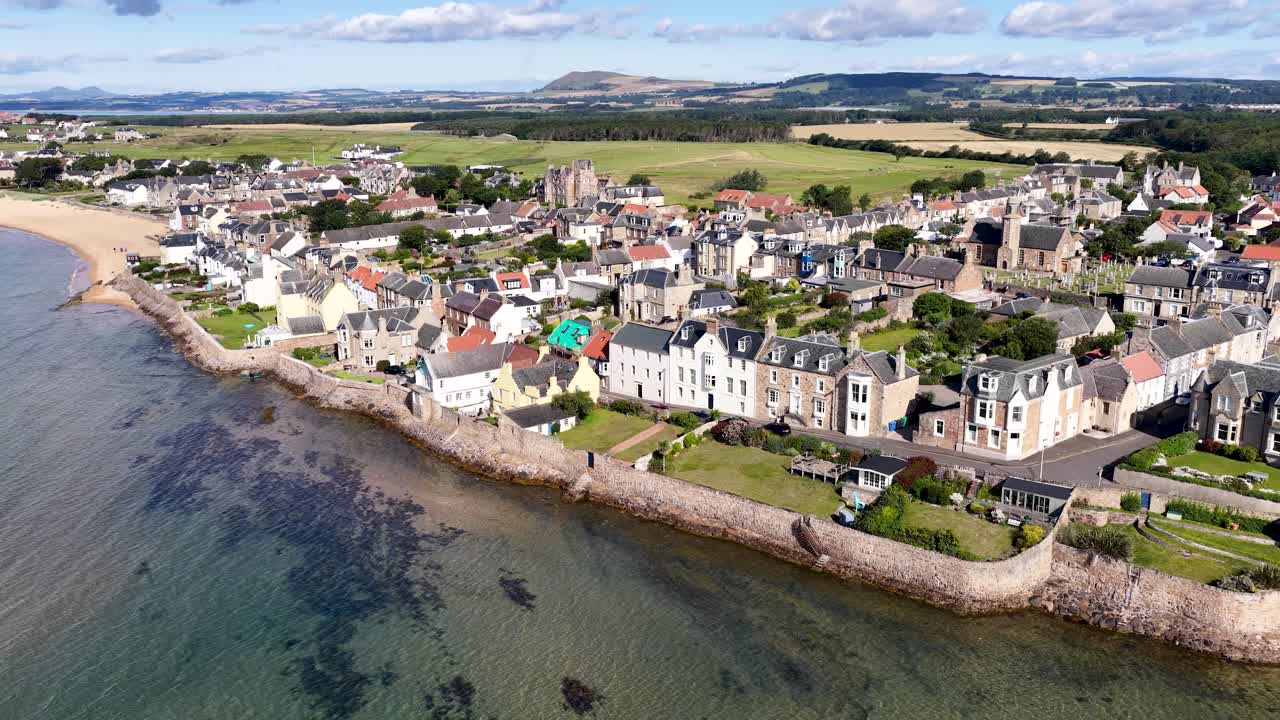 Drone glides above seaside village, revealing waterfront homes, sandy beach, and scenic summer landscape