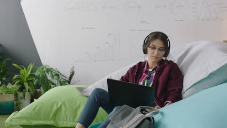 estudiante feliz usando computadora portátil digital navegando en línea mensajes de redes sociales lluvia de ideas proyecto creativo relajándose en almohadas coloridas escuchando música en una oficina moderna