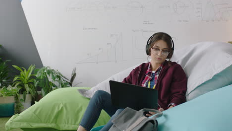 happy woman student using digital laptop computer browsing online social media messages brainstorming creative project relaxing on colorful pillows listening to music in modern office