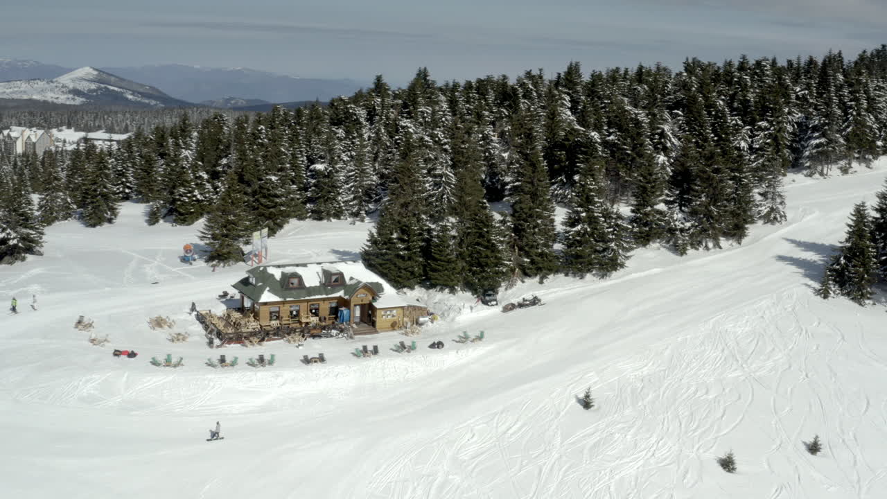 Aerial View of a Ski Resort with a Chalet and Skiers on a Sunny Winter Day