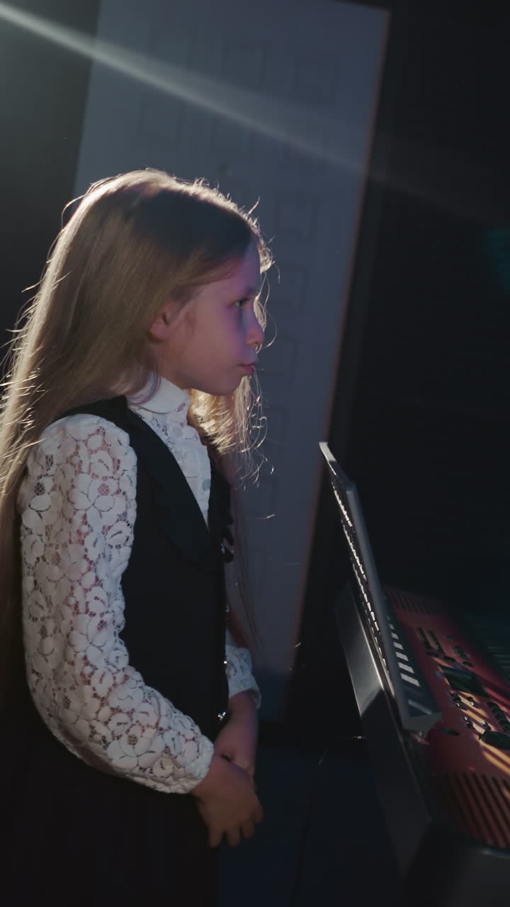 niño rubio y entrenador trabajan en un estudio de música. el hombre toca el sintetizador mientras la niña hace calentamiento vocal en una habitación aislada de sonido. lección de canto