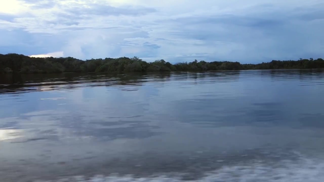 Superficie lisa de un río reflejando el cielo al atardecer, durante un paseo en barco. Vista amplia.