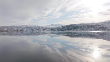 surface of water in fjord is dead calm with perfect reflection of sky