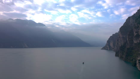 Un-Barco-Grande-Parece-Pequeño-Viajando-Por-El-Lago-Di-Garda,-Italia,-Con-Una-Luz-Matutina-Asombrosa-Y-Suave