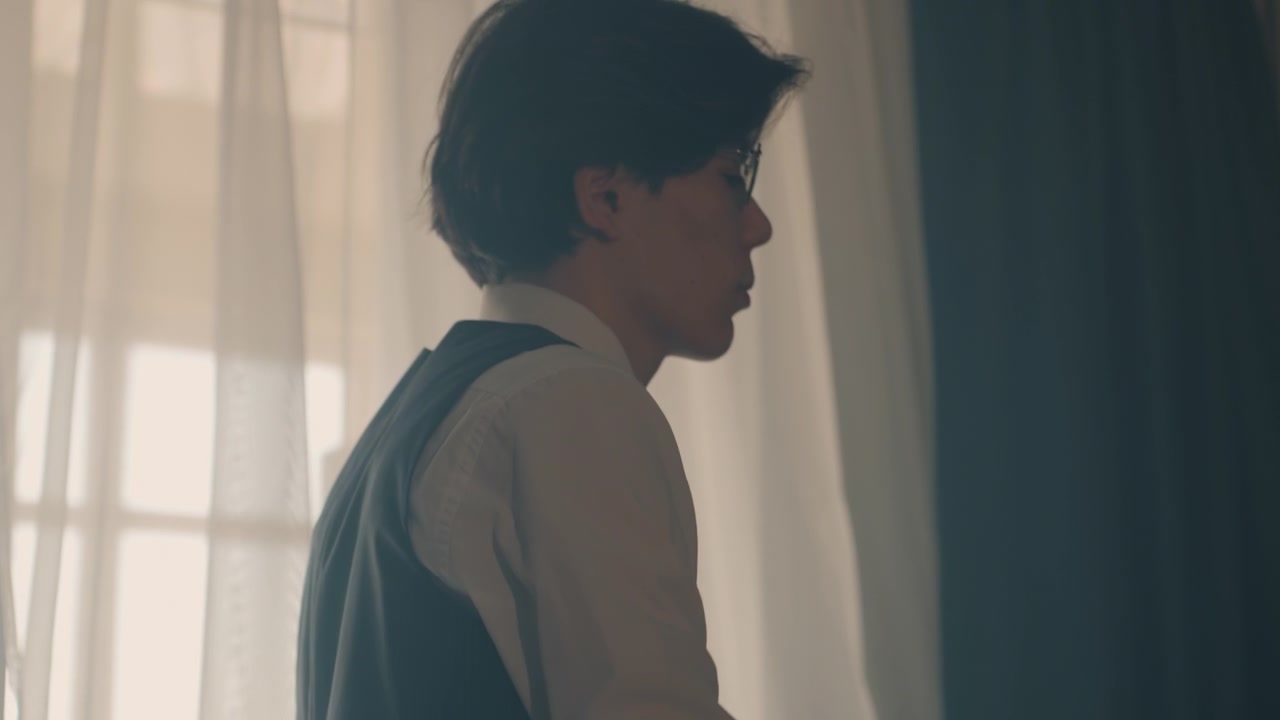 창가에서 옷을 입는 젊은 백인 남성, 재킷을 입고 소매를 조절하는 분위기 있는 영화 같은 아침, 부드러운 역광 커튼, 작은 침실의 책상과 의자, 학생 및 인턴 분위기, 사색적.