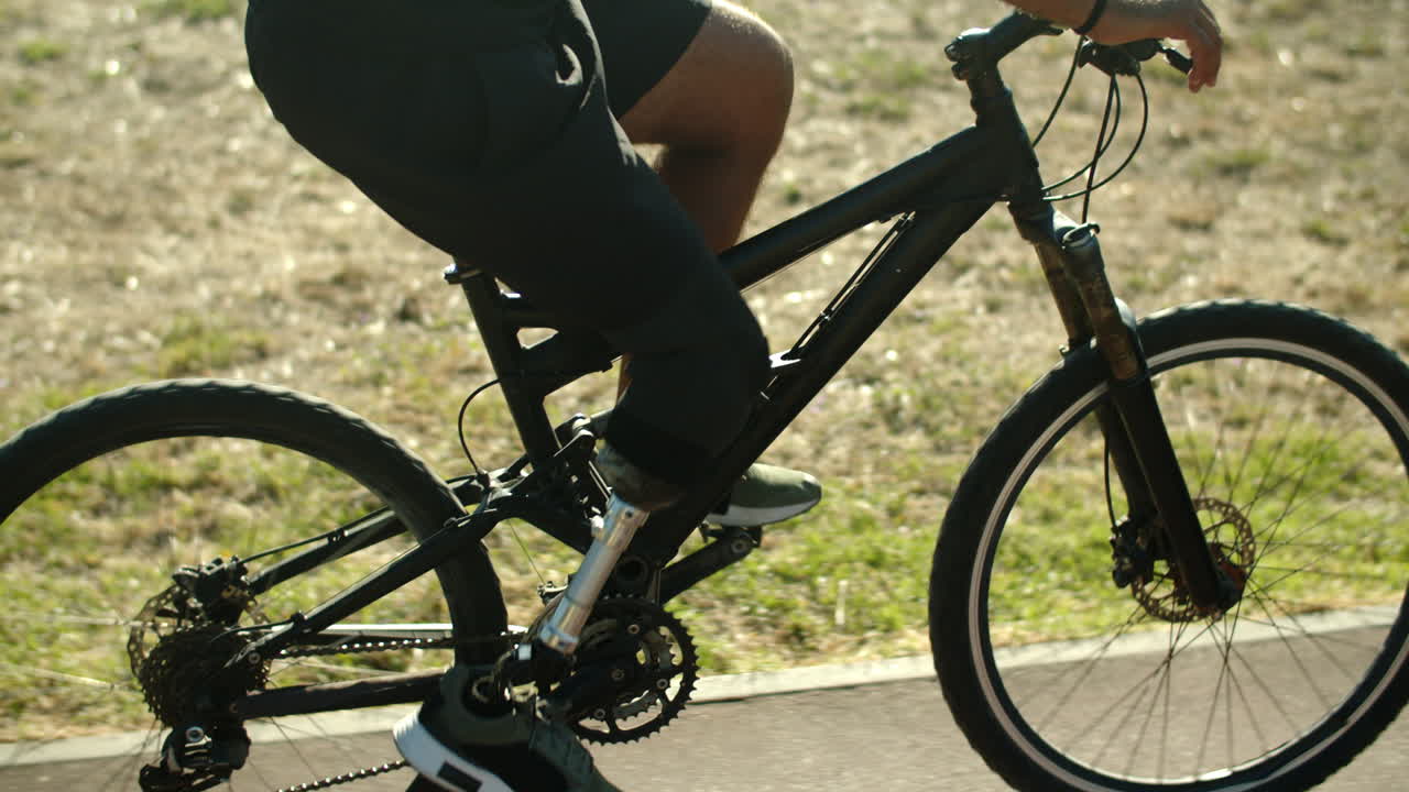 vista lateral de un hombre irreconocible con una pierna biónica en bicicleta en el parque
