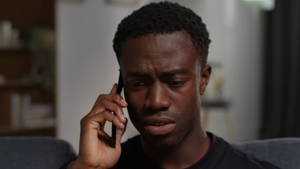 Unhappy And Depressed Young Man Sitting On Sofa At Home Ending Call After Talking On Mobile Phone 1