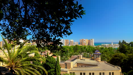 scenic view of málaga city from the gibralfaro fortress, with palm trees and historic architecture blending with modern buildings against a backdrop of the mediterranean sea