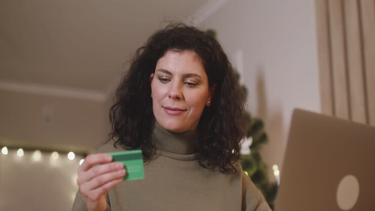 Bottom View Of Brunette Woman Buying Online With A Credit Card Using A Laptop Sitting At A Table In A Room Decorated With A Christmas Tree
