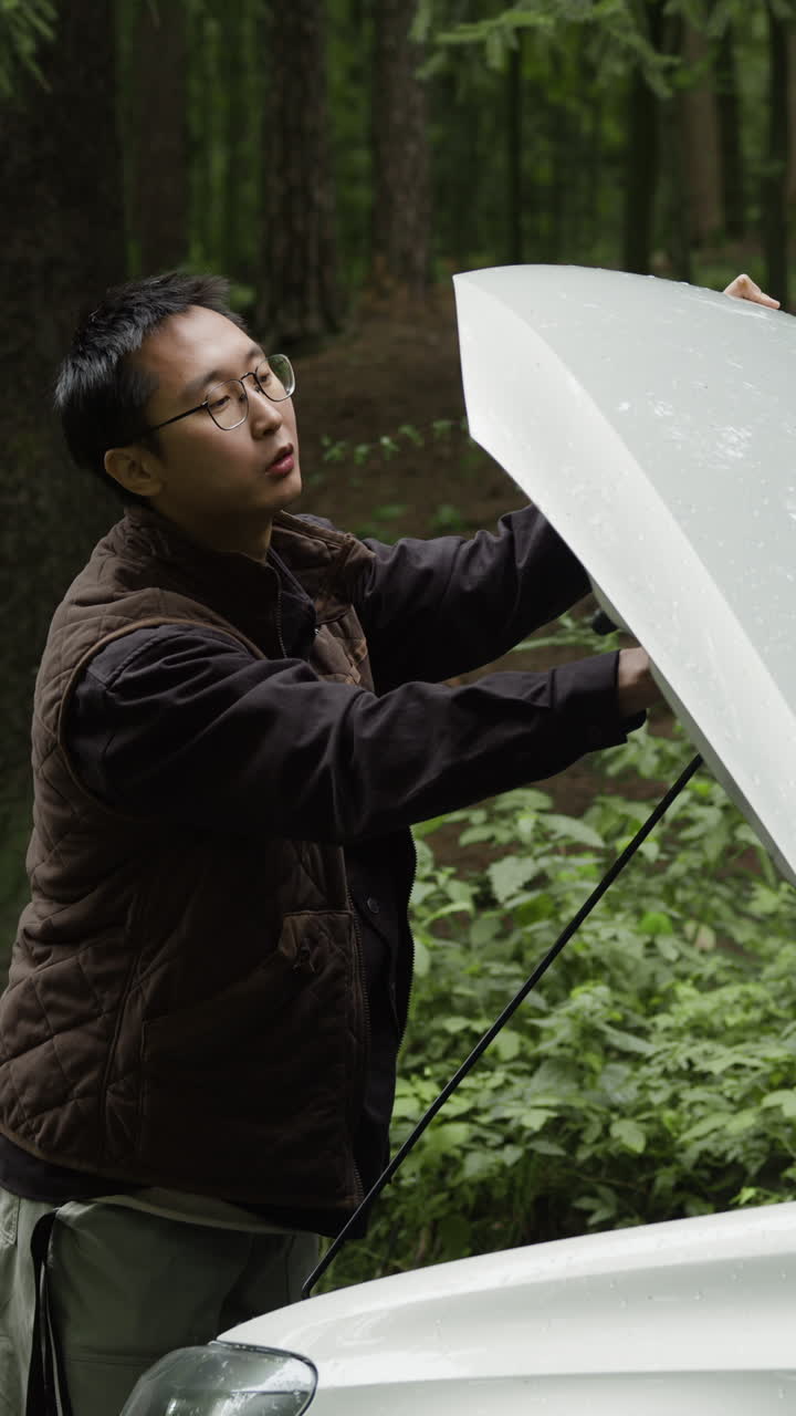 Man Inspecting Car Hood in Forest