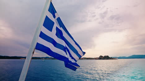 greek flag waving in the back of a ferry navigating along the coast of corfu in greece