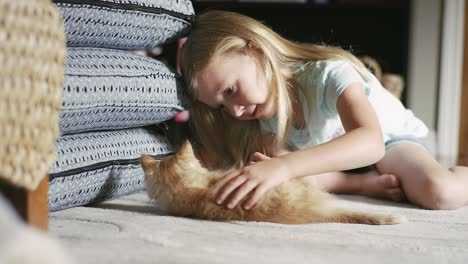 a little girl sitting on the floor and petting a kitten