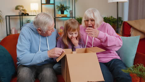 happy excited grandparents and granddaughter girl opening cardboard box unpack good parcel at home