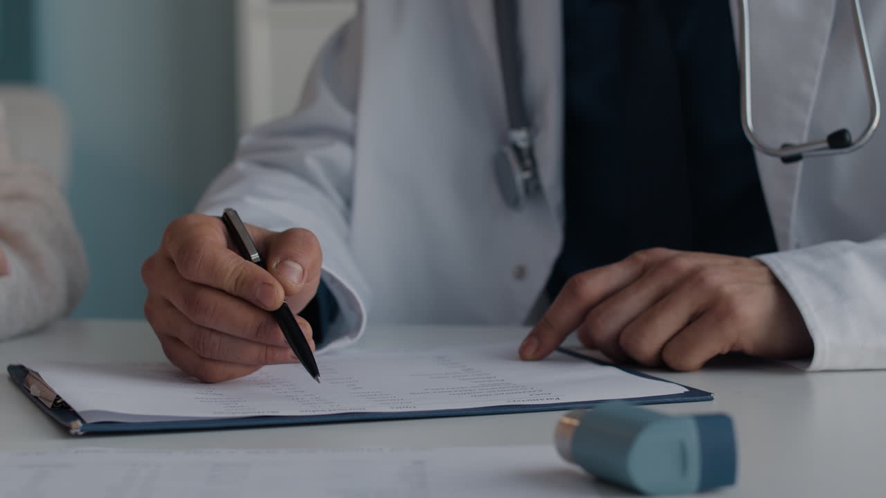 A doctor filling out medical records with an asthma inhaler on the table