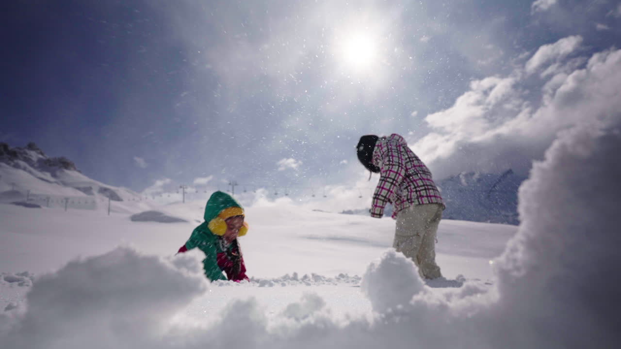 Static shot captures woman and her daughter joyfully throwing snowballs at each other on a clear sunny day at Las Leñas, Mendoza