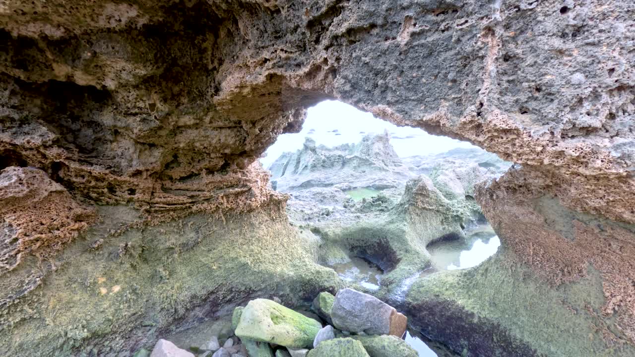A camera pans through a rocky coastal cave, revealing textured walls and scattered stones under natural light