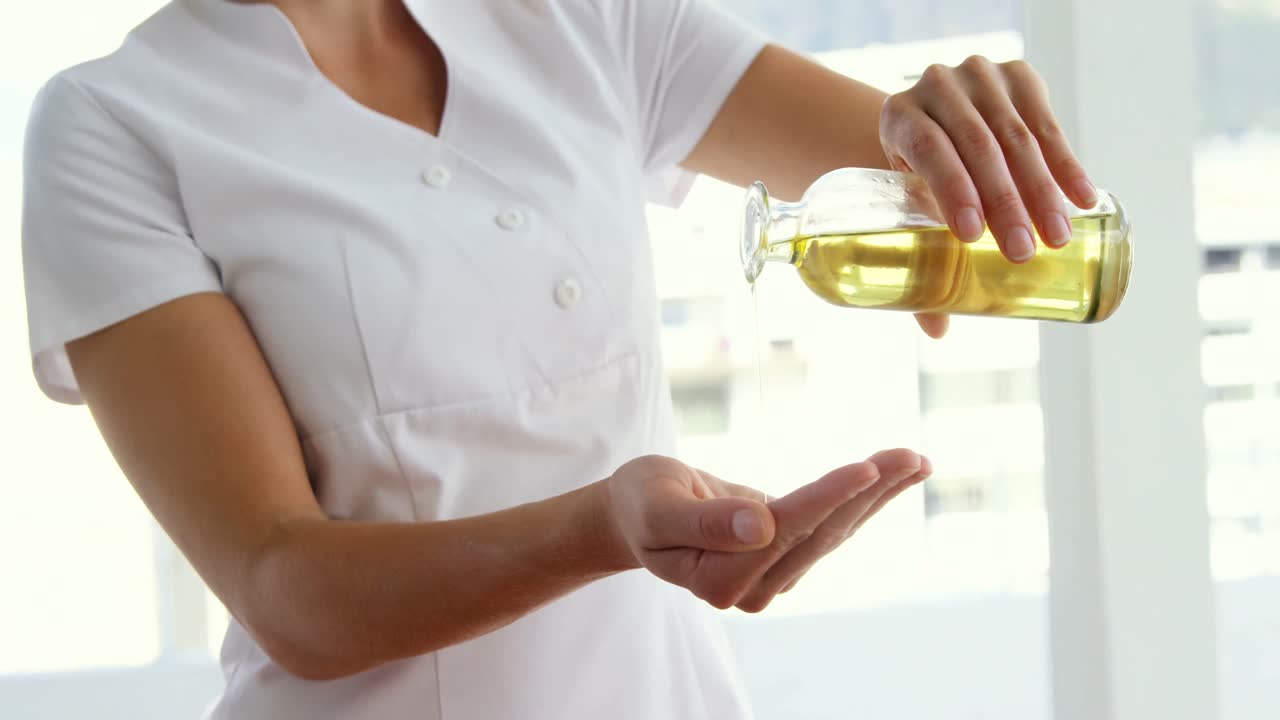 массажист наливает масла для массажа в ее руки.