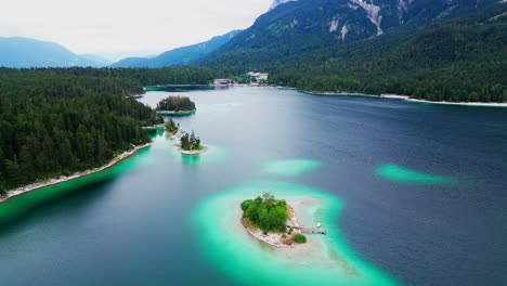 aerial view of a large colorful lake, surrounded by a vast field of pine trees, with mountains in the background