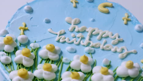 primer plano y zoom de un pastel de cumpleaños con glaseado azul, decorado con pequeñas flores blancas coronadas con puntas amarillas más acentos verdes