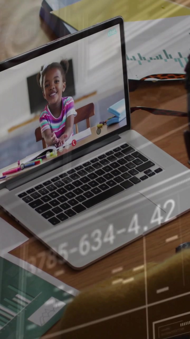 Vídeo vertical: Responsável em uma mesa participando de uma chamada educacional pelo laptop, com sobreposições HUD deslizando pela tela.