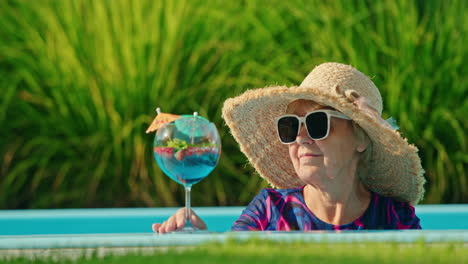 mujer mayor relajándose junto a la piscina con un cóctel