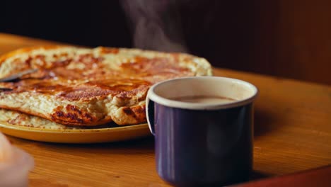 pouring fresh milk from carton into hot coffee in mug on table, plate of delicious pancakes in background. closeup shot