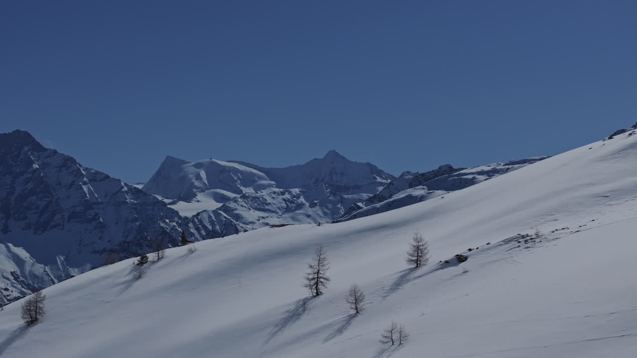 Rekaman aerial drone dari pegunungan yang tertutup salju di sekitar resor ski Bruson di Val de Bagnes Swiss pada hari musim dingin bluebird yang cerah, menampilkan lanskap alpine dan pemandangan musim dingin