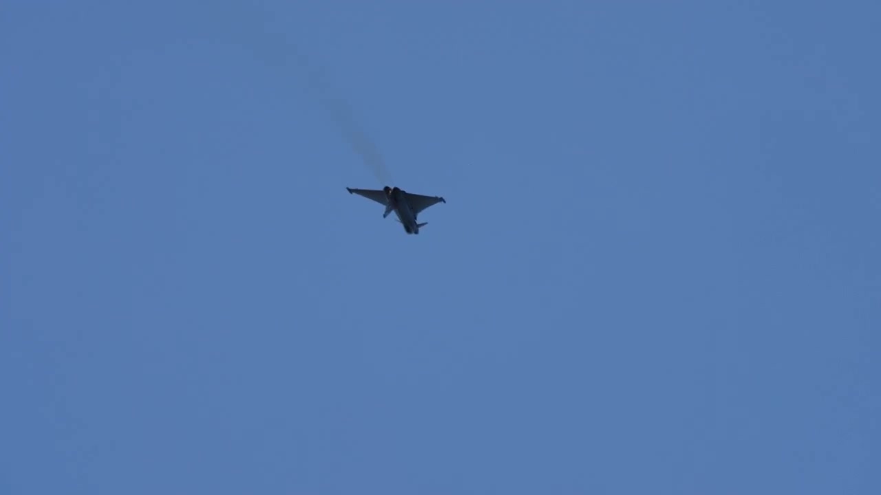 Militärischer Kampfjet führt einen steilen Vertikalaufstieg mit sichtbaren Nachbrennern am Himmel durch.