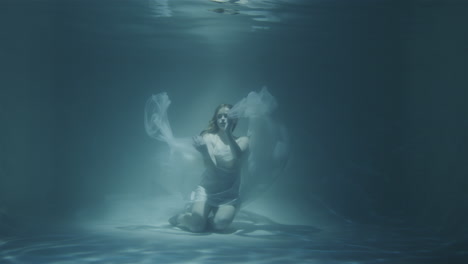 redhaired woman meditating underwater in white dress