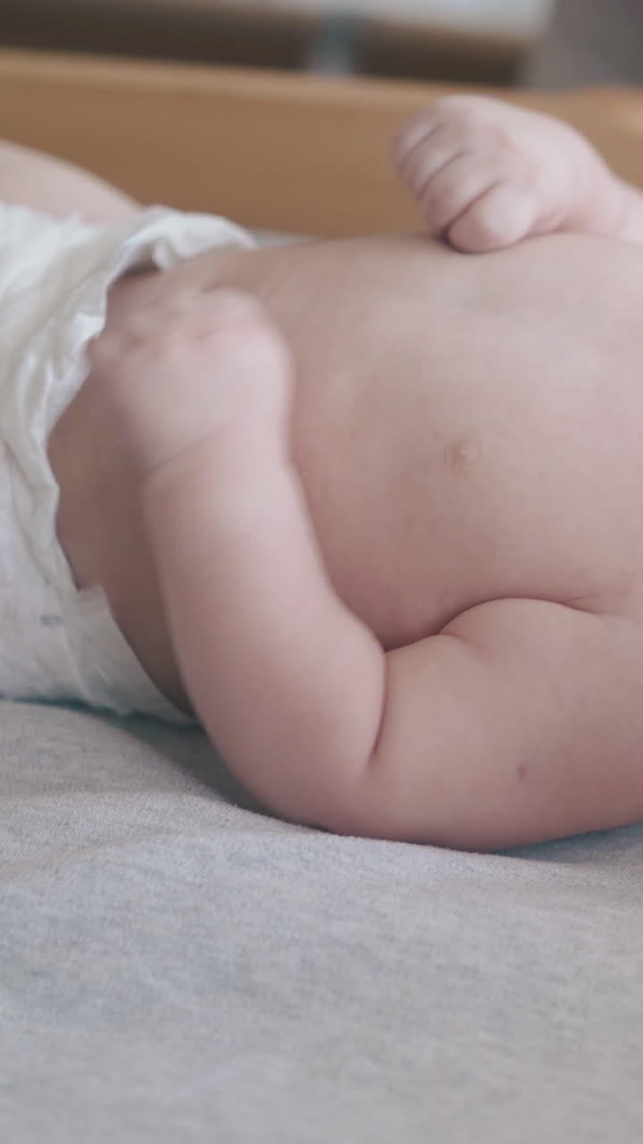 adorable fair haired newborn son lies on baby changing table and cries and nurse turns infant close view