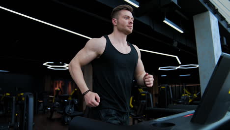 young handsome man training on a simulator. athletic guy is running on a modern treadmill in the gym. slow motion.