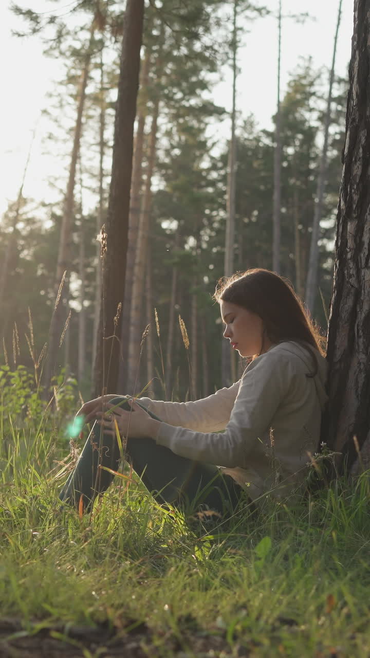 mujer se sienta apoyada en el tronco de un árbol en el bosque al atardecer. joven pensativa considerando la decisión de ir al psicólogo para mejorar la salud mental. paseo nocturno en el bosque