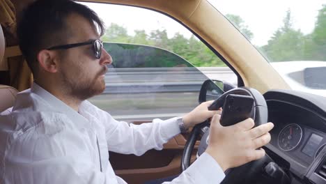 businessman driving a car looks at the phone in traffic.