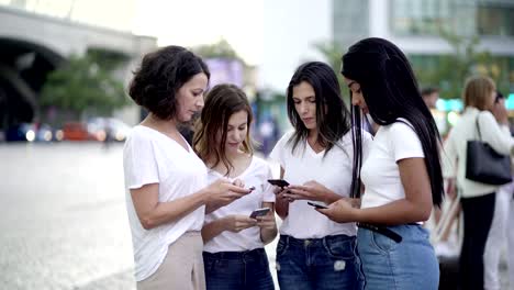 amigas concentradas de pie en la plaza con teléfonos