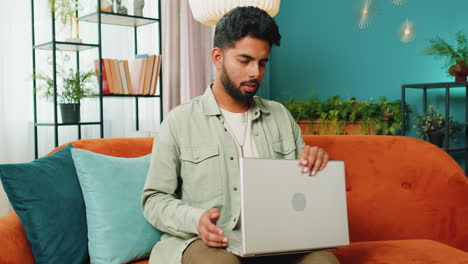 Young-man-freelancer-sitting-on-couch-closing-laptop-pc-after-finishing-work-in-living-room-at-home