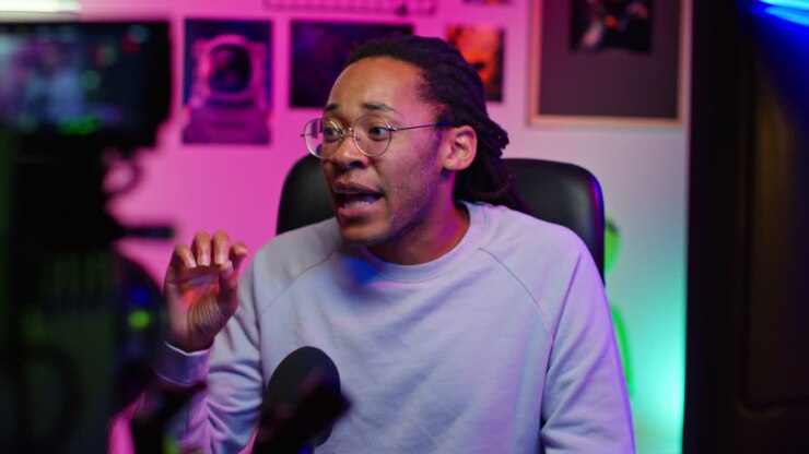 Uomo con dreadlocks e occhiali che registra un video nel suo studio casalingo